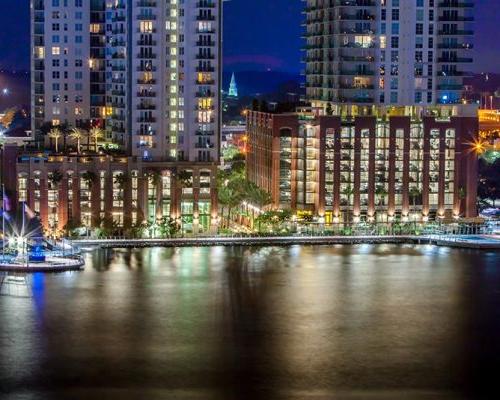 Photo of Jacksonville's Southbank Riverwalk at night from across the river. Building lights reflect off the water.